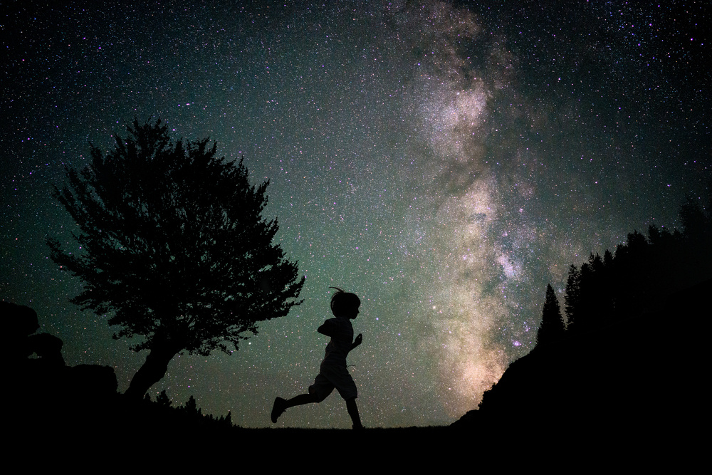 Happy child running silhouette with Milky Way and beautiful night sky full of stars in background